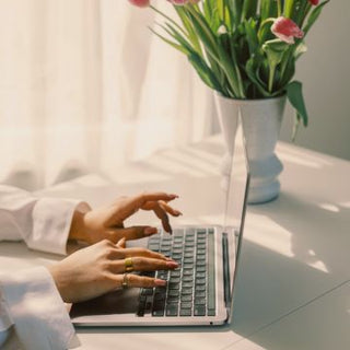 Person using a laptop to do a personal styling session and consultation with mylene amelie. There is a vase of flowers on a table