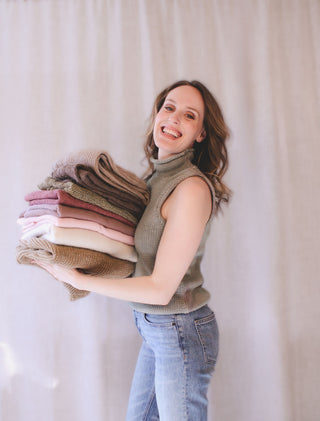 Personal stylist Mylène Amelie holding a stack of knit sweaters during a wardrobe styling session, helping clients build cohesive outfits and curated wardrobes in Calgary and through virtual styling services.