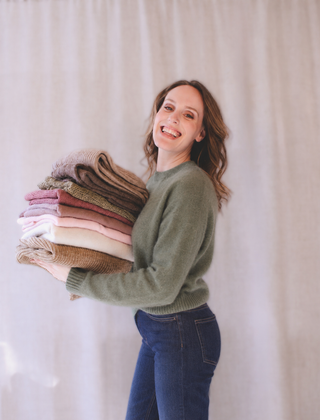 Personal stylist Mylène Amelie holding a stack of knit sweaters during a wardrobe styling session, helping clients build cohesive outfits and curated wardrobes in Calgary and through virtual styling services.